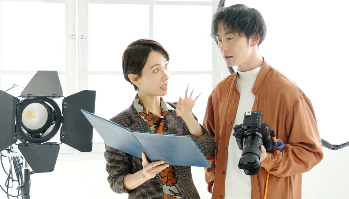 撮影現場でデザインレイアウトを確認しながら打ち合わせるデザイナーとカメラマン